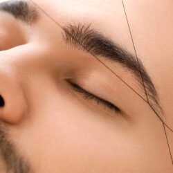 Young man undergoing eyebrow correction procedure in beauty salo